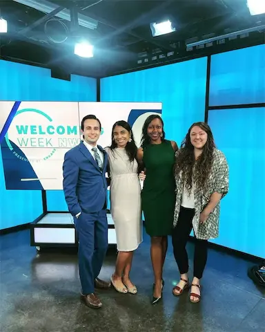 Group of four people smiling on a TV set with Welcome Week NW displayed on monitors.