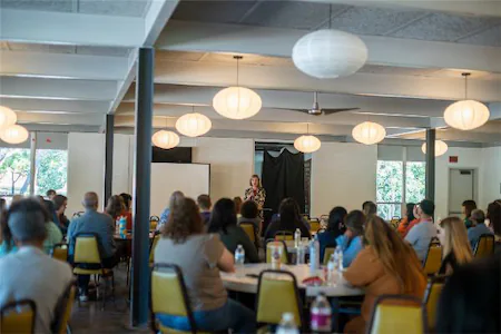 People attending a seminar in a well-lit room with round tables and hanging lamps.