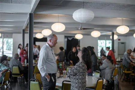 Networking event in a modern venue with people engaged in conversation and seated at tables under globe lights.