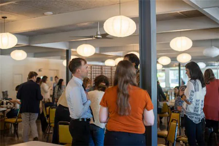 People networking at a conference in a bright, modern venue with hanging lights and open seating.