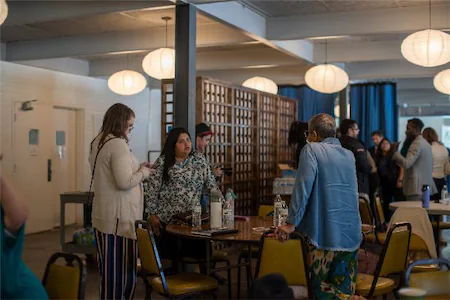 People socializing and conversing in a warmly lit room with hanging lights and tables.