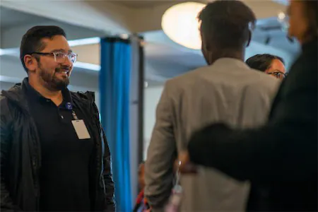 Group of professionals networking at an indoor event, engaging in conversation with smiles and attentive expressions.
