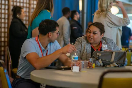 Two people engaged in conversation at a conference table, holding water bottles and wearing name badges.