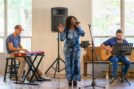 Singer performing with musicians on keyboard and guitar in a bright room setting.