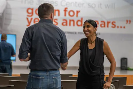 People shaking hands at a business event with a motivational quote in the background.