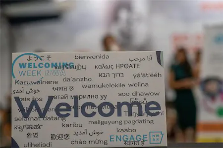 Multilingual welcome sign highlighting cultural diversity at an event with blurred people in the background.