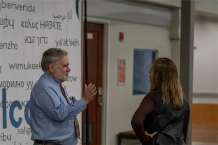 Two people talking in a hallway with a multilingual welcome banner in the background.