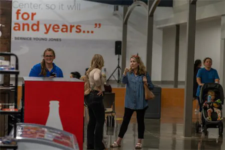 People interacting in a busy indoor common area with a quote on the wall in the background.