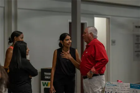 Four people engaged in conversation indoors, one wearing a red shirt, with a welcoming atmosphere.