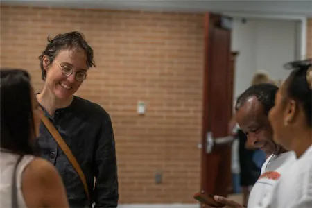 A group of people engaging in conversation indoors with brick wall background.