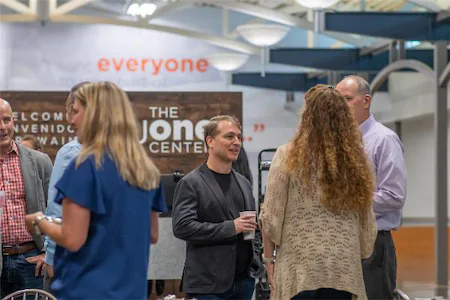 People networking in a community center with everyone sign, engaged in conversation and holding coffee cups.