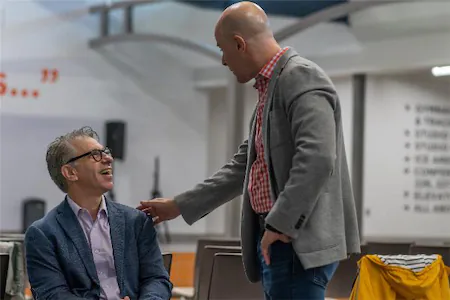 Two men in a lively conversation, smiling in a modern, open space with casual seating and professional attire.