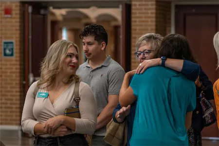 People gathering in a hallway, with some hugging and others conversing, creating a warm and social atmosphere.