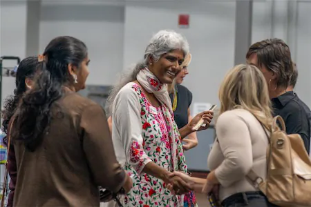 Group of diverse people engaged in conversation and smiling at an event indoors.