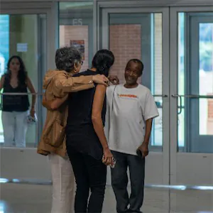 Group of people happily chatting and smiling near large glass doors in a bright, indoor setting.