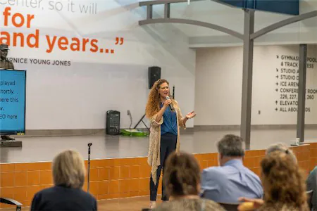 Speaker giving a presentation in a conference room with an audience and quote on the wall in the background.