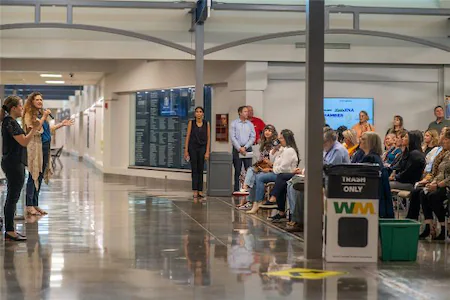 Person presenting to a seated audience in a hallway, engaging in a public speaking or educational event.