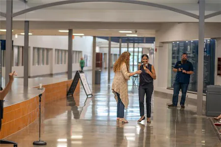 People talking and holding a microphone in a hallway with others observing, reflecting a collaborative atmosphere.