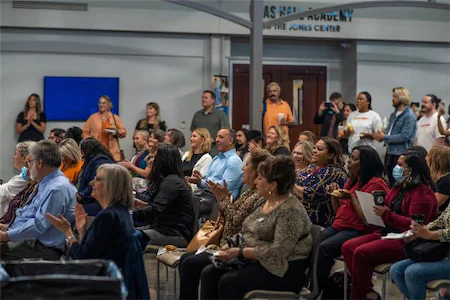 Audience attentively listening at an indoor event with seated and standing participants.