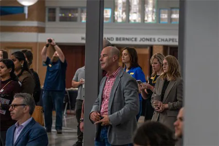 People attending an event at Harold and Bernice Jones Chapel, with some holding phones and others listening attentively.