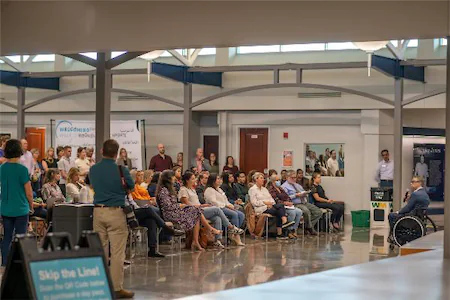 Audience attentively listening to a speaker in a wheelchair during a seminar in a modern conference hall.