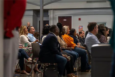 Audience attentively listening to a speaker at a conference in a spacious hall, focusing on business and networking.