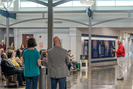 Speaker addresses audience in a modern, industrial-style conference hall with attendees seated and engaged.