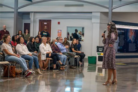 Speaker addressing a seated audience in a spacious hall.
