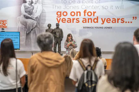 Woman speaking to audience at the Jones Center event, featuring a backdrop with Bernice Young Jones quote.