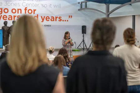 Speaker addressing audience in a conference hall with a quote displayed on the screen above.