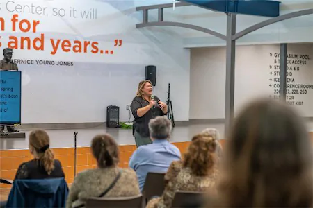 Speaker presenting to an audience in a community center with inspirational quote on the wall.
