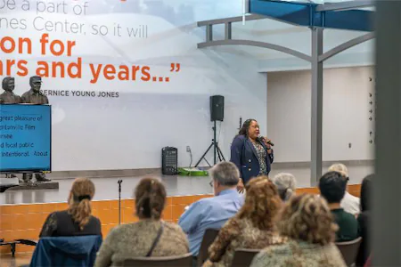 Speaker presenting to audience in a modern conference room with quote and two statues in the background.