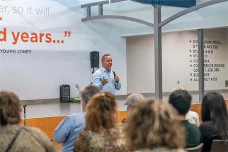 Speaker addressing an audience in a modern conference room setting with motivational quote on the wall.