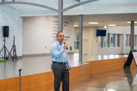Man speaking into a microphone in a modern building with orange and white interior design.