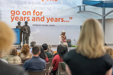 Audience listening to a speaker at The Jones Center event with a statue and quote in the background.