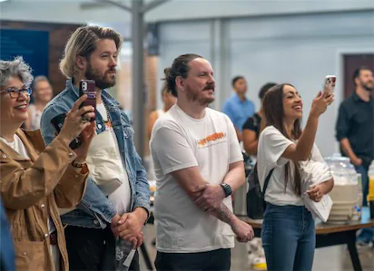People at an indoor event capturing moments with smartphones, smiling and engaged in the surroundings.
