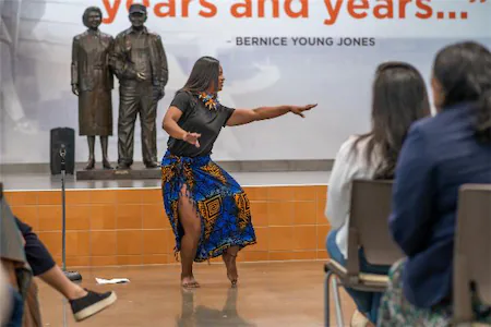 Dancer performs in front of seated audience at cultural event, colorful skirt, historical statue backdrop.