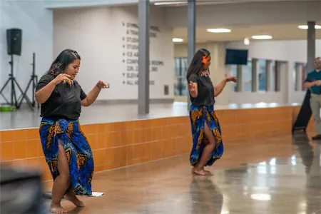 Two dancers in colorful skirts perform indoors, showcasing traditional cultural dance moves.