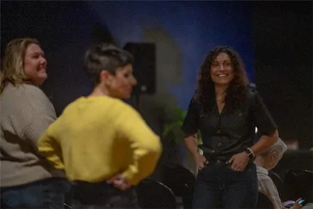 Three people smiling and chatting in a dimly lit room.