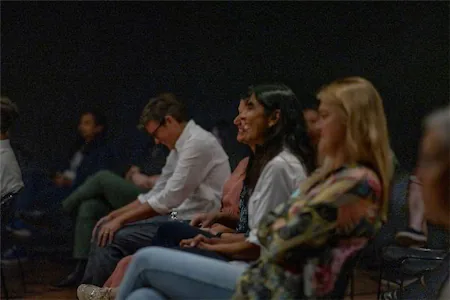 Audience attentively watching a presentation, seated in rows with a dark background.