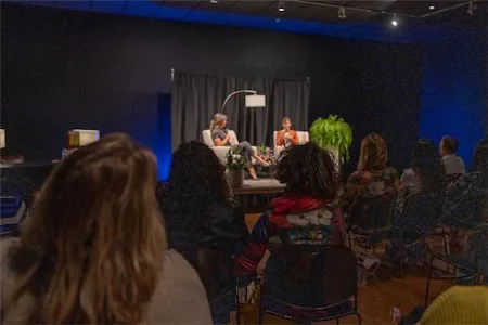 Audience watching an engaging live talk show with two speakers on stage in a dimly lit studio.