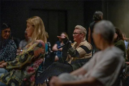 Audience member asking a question at a seminar, surrounded by attentive listeners in a dimly lit room.