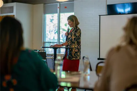 Person giving a presentation in a bright room with attendees listening attentively.