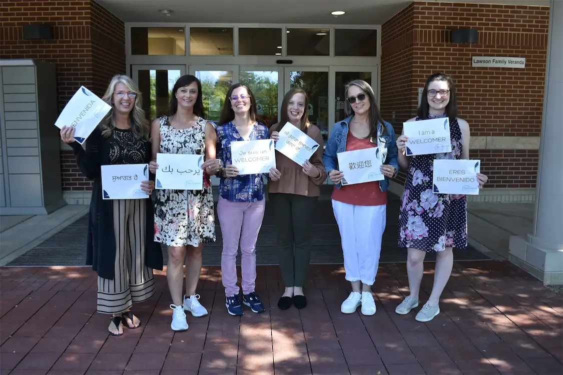 Group of people holding multilingual welcome signs outside a building entrance.