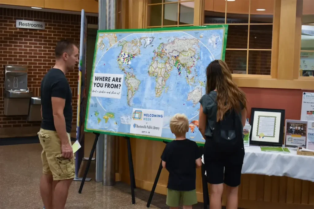 People exploring a world map display at Bentonville Public Library during Welcoming Week.