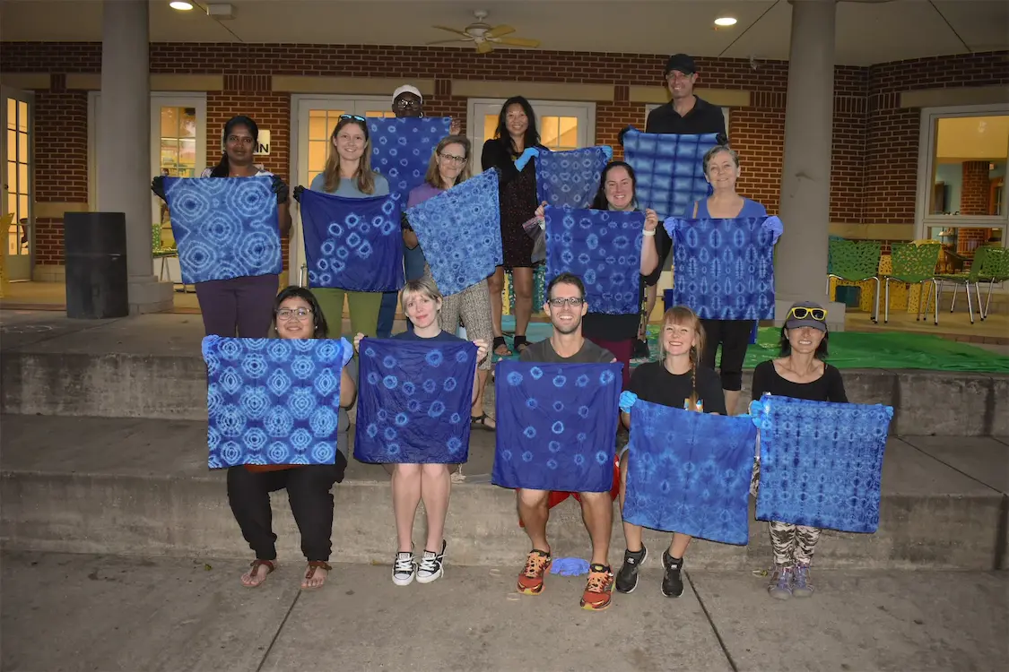 Group displaying blue tie-dye fabric art on steps outside a building.
