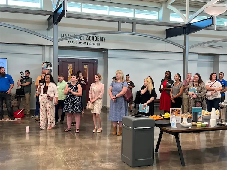Group of people attending an event at a academy with refreshments on a table in the foreground.