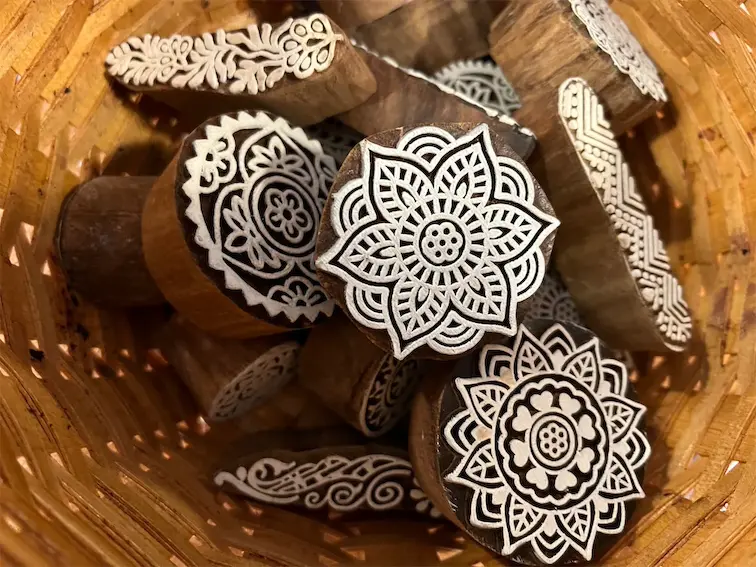 Wooden block stamps with intricate floral designs in a basket, ideal for textile and craft printing.