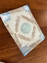 Decorative book with intricate floral design and blue accents on a wooden table.