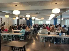 People attending a workshop in a modern, spacious conference room with round hanging lights and large windows.